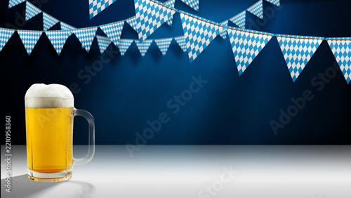 Mug of foamy beer on a white surface and blue-and-white checkered pennants hanging against a dark blue wall. Perfect for Bavarian festival promotions and party invitations.