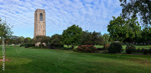 Wide panoramic view of a lush green city park featuring a historic stone carillon tower in Frederick, Maryland, under a beautiful patterned cloud sky.