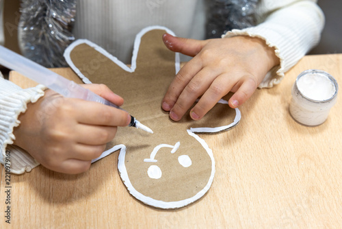 Little girl's hands, child decorating, painting gingerbread man made from cardboard. Christmas preparation. Concept of eco holiday, New year eve, family, motherhood and childhood