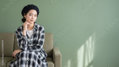 ベレー帽とチェック柄シャツを着てソファに座る女性