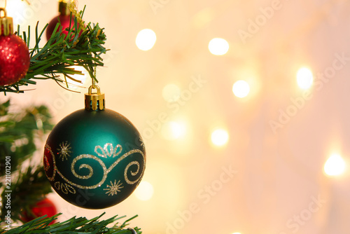 Decorated christmas tree branch hanging green ball ornament bringing joyful festive holiday spirit with bright light bokeh background creating warm cheerful feeling for seasonal celebration