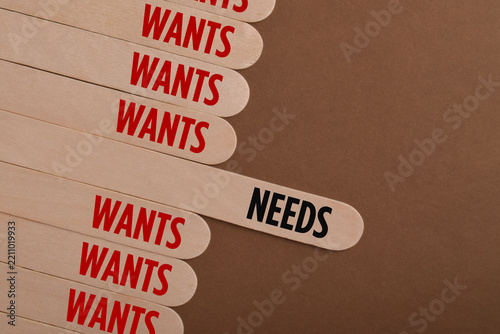 Wooden sticks labeled needs and wants illustrate consumer priorities, purchasing decisions, budgeting, financial planning, and the difference between essentials and desires.