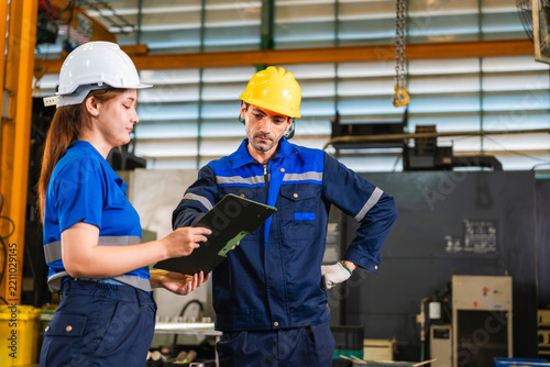 Factory workers reviewing production report on clipboard in manufacturing plant, industrial engineers in safety gear discussing quality control data in workshop