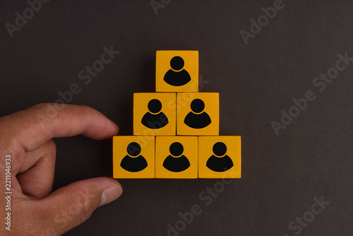 Fotografie Yellow blocks with people icons form a leadership pyramid while a hand points toward the structure, representing hierarchy, management, teamwork, authority, and organizational roles