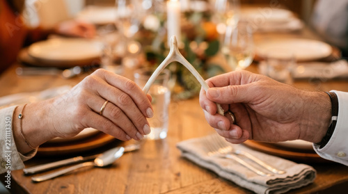 Festive background shows two hands holding wishbone over wooden table creating hopeful and joyful moment during holiday gathering