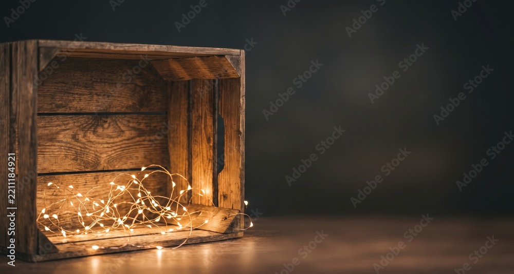 Fototapeta premium Empty rustic wooden crate with glowing warm fairy lights inside, set against a dark background, with copy space, on the right side