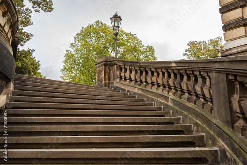 Close-up of an ornate architectural staircase with carved sandstone balustrade, weathered masonry, decorative columns and vintage metal fencing.