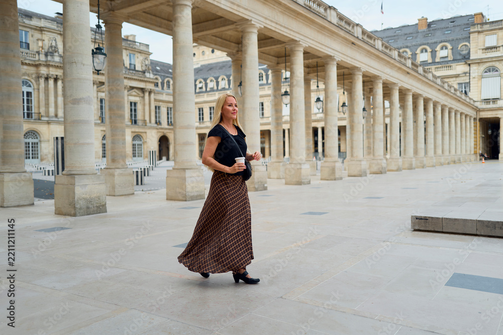 Obraz premium Blonde woman with coffee walks through Paris courtyard