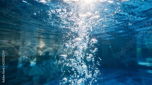 Clear blue pool water with a burst of airy oxygen bubbles floating towards the bright surface area.