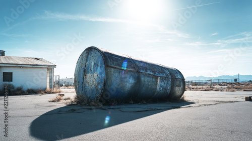 Rusty industrial storage tank abandoned on cracked asphalt in a desolate, forgotten desert landscape