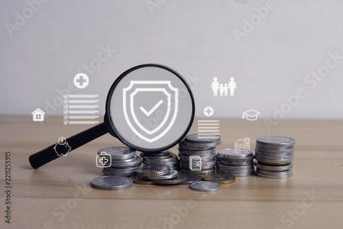 Closeup of Stacks Coins Under Magnifying Glass Displaying Insurance Shield Hologram