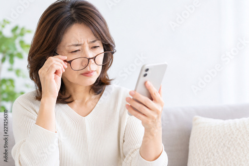 スマートフォンの文字が見づらくメガネをずらして確認する中年女性