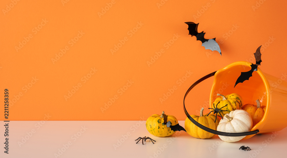 Obraz premium Happy Halloween scene with pumpkin, spider and bat spilling from orange bucket on orange background with empty space