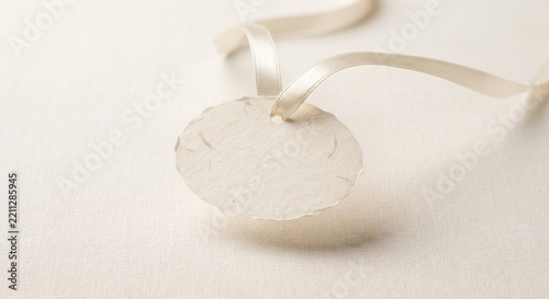 A blank round white paper gift tag hanging from a simple light ribbon against a soft background