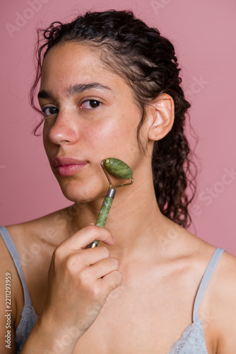 Hispanic woman with jade roller massaging face in beauty shoot
