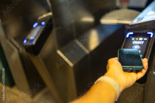 Obraz na plátně Hand holding a smartphone near a subway turnstile reader, using contactless paym