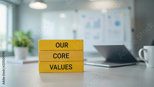 Three yellow wooden blocks stacked on a desk showing the text our core values with stacked vertically bright printed them stacked office desk laptop professional