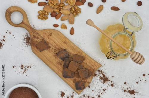 Baking ingredients for baking with chocolate: chocolate chunks on a wooden tray, mixed nuts and almonds, cocoa powder and honey in a glass jar on a kitchen table. Brown and yellow elements.