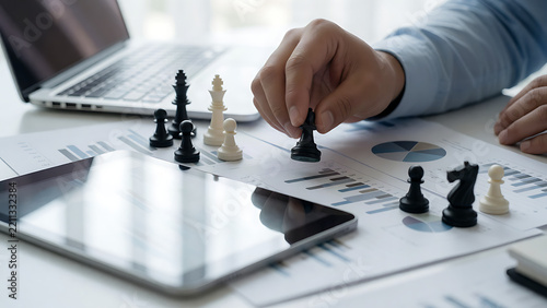 Businessman playing chess on financial documents with laptop and tablet