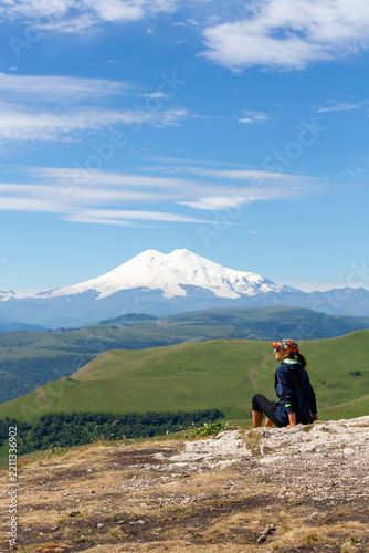 A female tourist sits on rocks and looks at Mount Elbrus in the North Caucasus