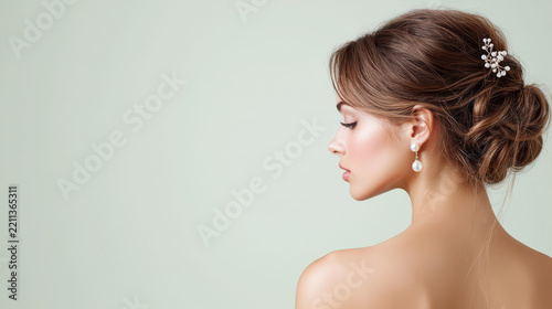 Elegant portrait of woman with stylish updo, showcasing pearl accessories and soft makeup against light background