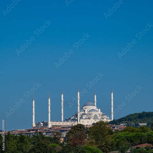 Wide outdoor view of grand mosque complex with multiple slender minarets and central dome rising above buildings and green hills in Istanbul.