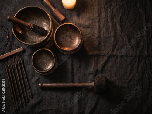 Brass bowls with striker and dark chimes by candlelight on rustic black fabric