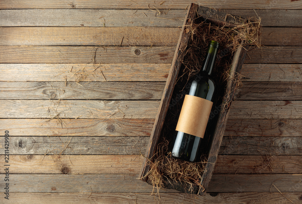 Obraz premium Bottle of red wine with empty label in an antique wooden box with hay.