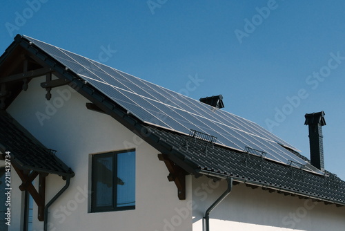 Large rooftop solar panel system on a modern residential house under clear blue sky, illustrating renewable electricity, energy independence and sustainable home power.