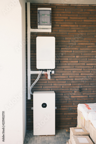 Residential solar energy storage system with wall mounted inverter, electrical distribution panel and home battery installed against a brick wall for backup power.