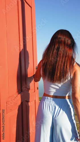 Woman opens a freestanding red door revealing a scenic sea view. Opportunity, freedom, new beginnings, discovery and life Woman opens a freestanding red door revealing a scenic sea view.