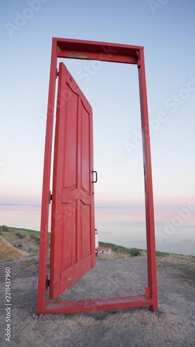 Freestanding red door slowly opens on a seaside landscape at sunset. Opportunity, new beginnings, freedom, transition and discovery concepts. Vertical video.