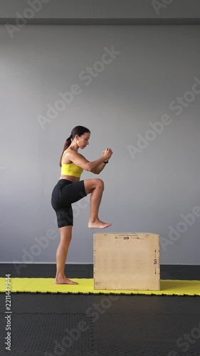 Athletic woman performs fast step-ups on a plyo box indoors. Leg strength, speed, coordination, functional fitness and athletic training concepts. Vertical video.