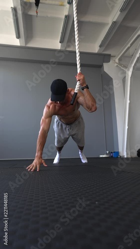 Muscular man performs one-arm push-ups while holding a rope indoors. Strength, calisthenics, grip training and athletic performance concepts. Vertical video.