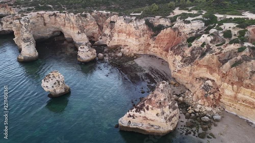 Sand beach among rocks on evening sunset. Ursa Beach near Arcos Naturais da Praia da Marinha at Atlantic Ocean coast in Portugal. Summer landscape. 