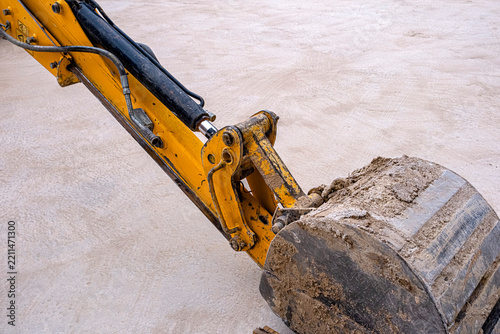 Close-up of a yellow excavator bucket and dirty hydraulic arm resting on a concrete surface. This industrial image is perfect for construction, engineering, heavy machinery, and urban development proj