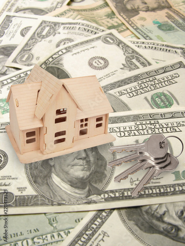 Keys and small wooden house are on many american dollars, collage - Mini house rests on scattered US dollar bills. Keys lie beside the house, symbolizing ownership