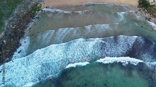 Aerial top view of ocean waves crashing on Meron Beach sand