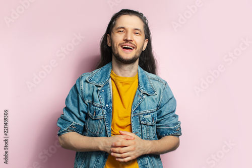 Portrait of excited happy young man with long hair on pastel pink background.