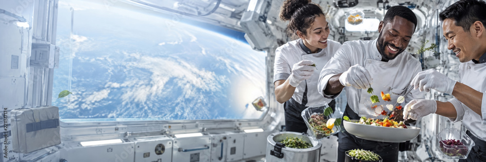Fototapeta premium Diverse astronaut crew prepares fresh food together inside a space station kitchen, with Earth visible through the window. Teamwork and healthy living concept.