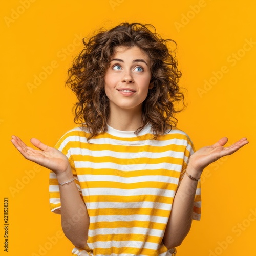 Young Woman with Curly Hair Wearing Yellow and White Striped T-shirt Standing Against Bright Orange Background