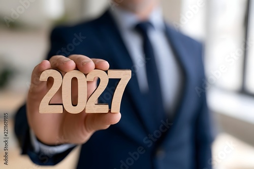 A person in a suit holds wooden cutout numbers spelling 2027  symbolizing future planning or upcoming goals