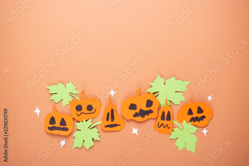 Halloween paper craft border with jack o lanterns and green leaves on orange background with copy space