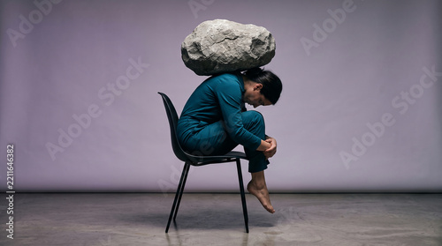 Woman with stone on head sitting on chair, symbolizing burden, stress, and struggle.