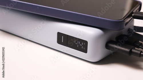 Smartphone connected to a portable power bank with multiple charging cables and a digital battery display on a white background