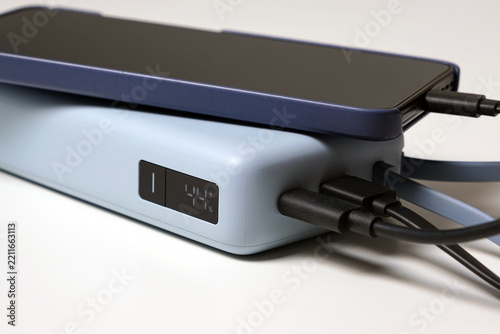 Smartphone connected to a portable power bank with multiple charging cables and a digital battery display on a white background
