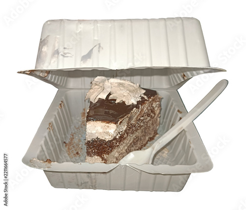 A single slice of layered chocolate cake with frosting inside an open white plastic takeaway box with a plastic spoon, isolated on white background.