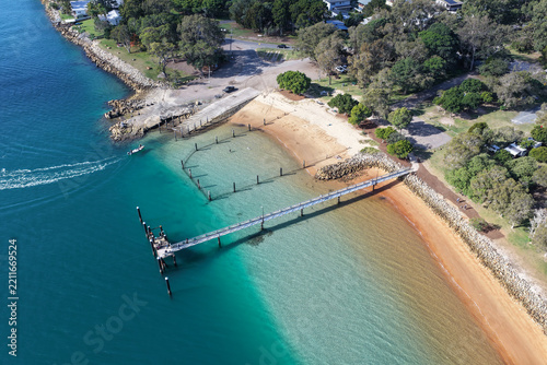 Aerial view of the jetty at Amity Point extending into the turquoise waters of Moreton Bay with a sandy beach and coastal vegetation in Amity Point, Queensland, Australia.