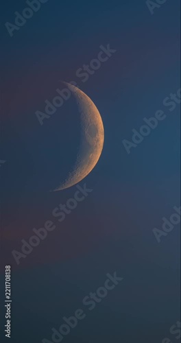 Vertical 9:16 time lapse of beautiful detailed golden crescent moon moving in twilight blue sky with pink clouds
