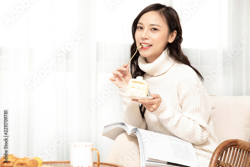 Happy Woman Eating Cake and Reading a Book at Home